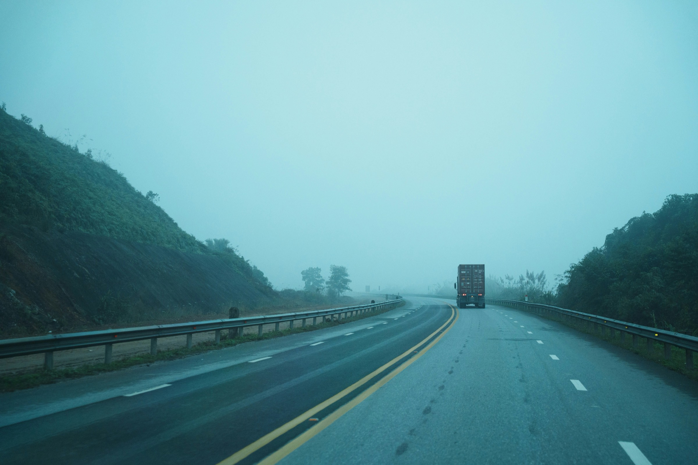 A container truck receding into highway fog at dawn, the delivery leg behind every order dispatched.